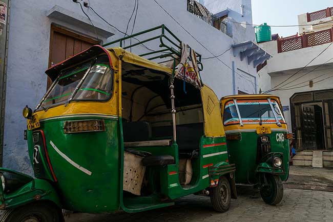 Two parked tuk-tuks on street.