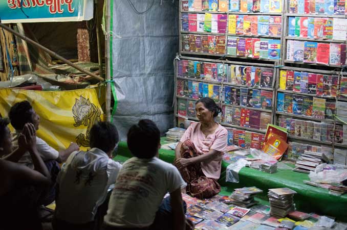 Woman selling books at night in market.