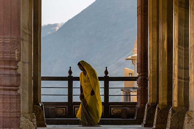 Woman in yellow sari sweeping.